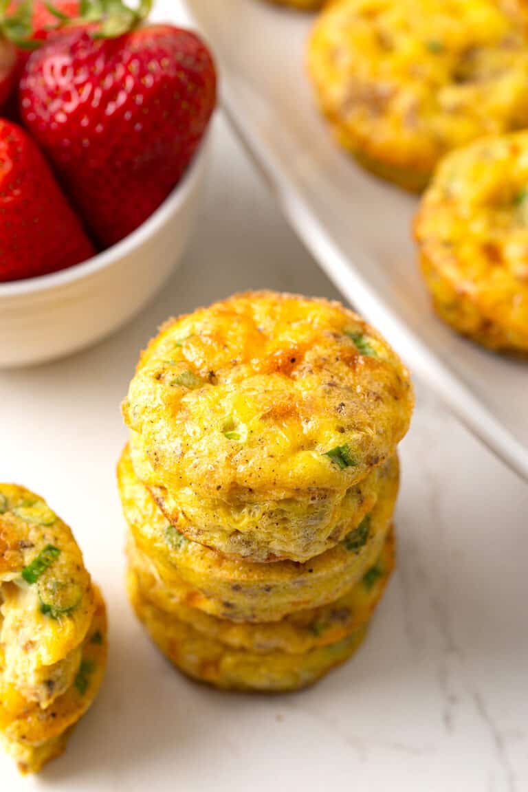 A stack of eggs muffins on a marble tabletop with strawberries in the background.