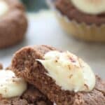 Titled image of two keto gingerbread thumbprint cookies on a white table, with a bite taken out of one.