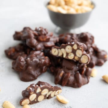 Keto Peanut Clusters piled up on a table with a bowl of peanuts in the background.