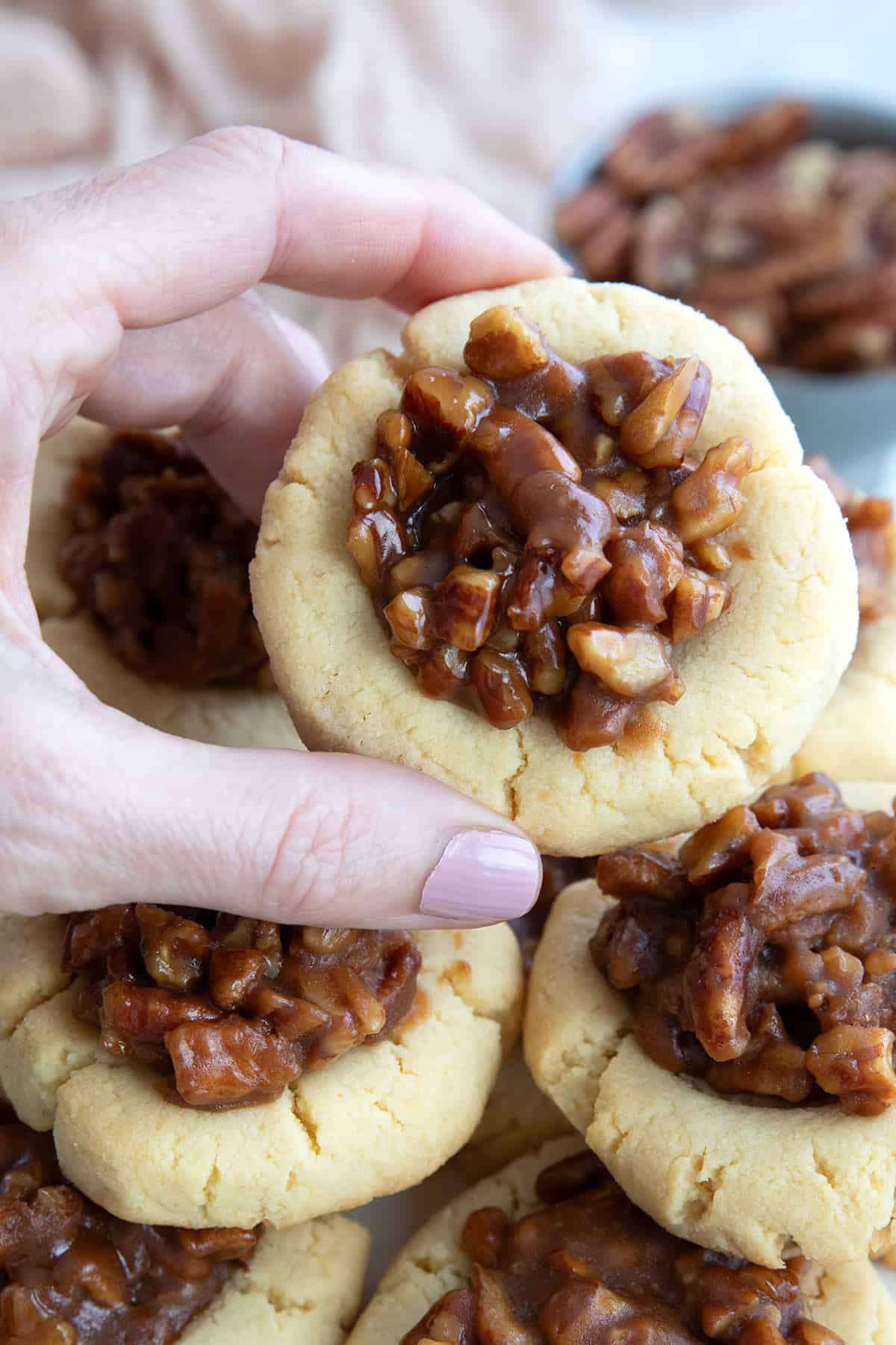 A hand holding up a Keto Pecan Pie Cookie over a plate of more cookies.