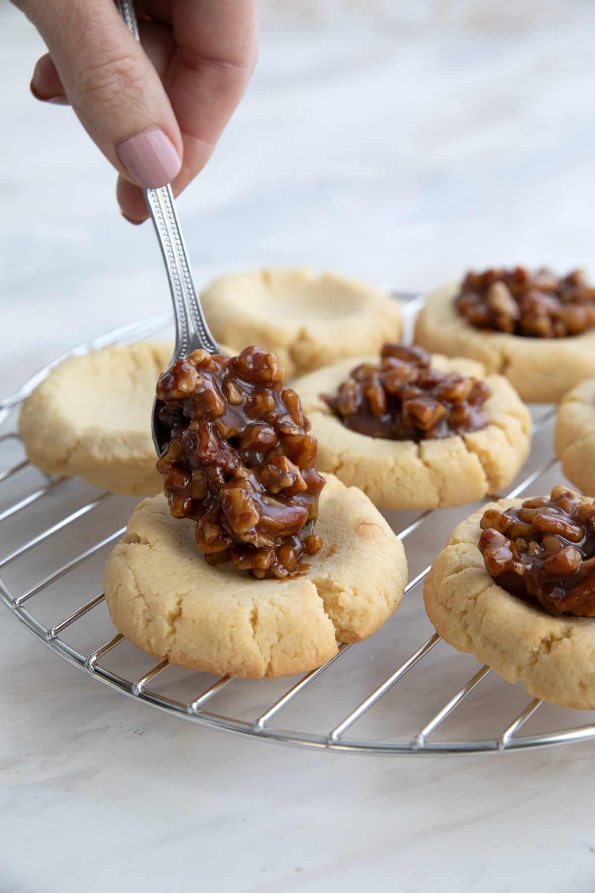 A hand spooning keto pecan pie filling into a thumbprint cookie.