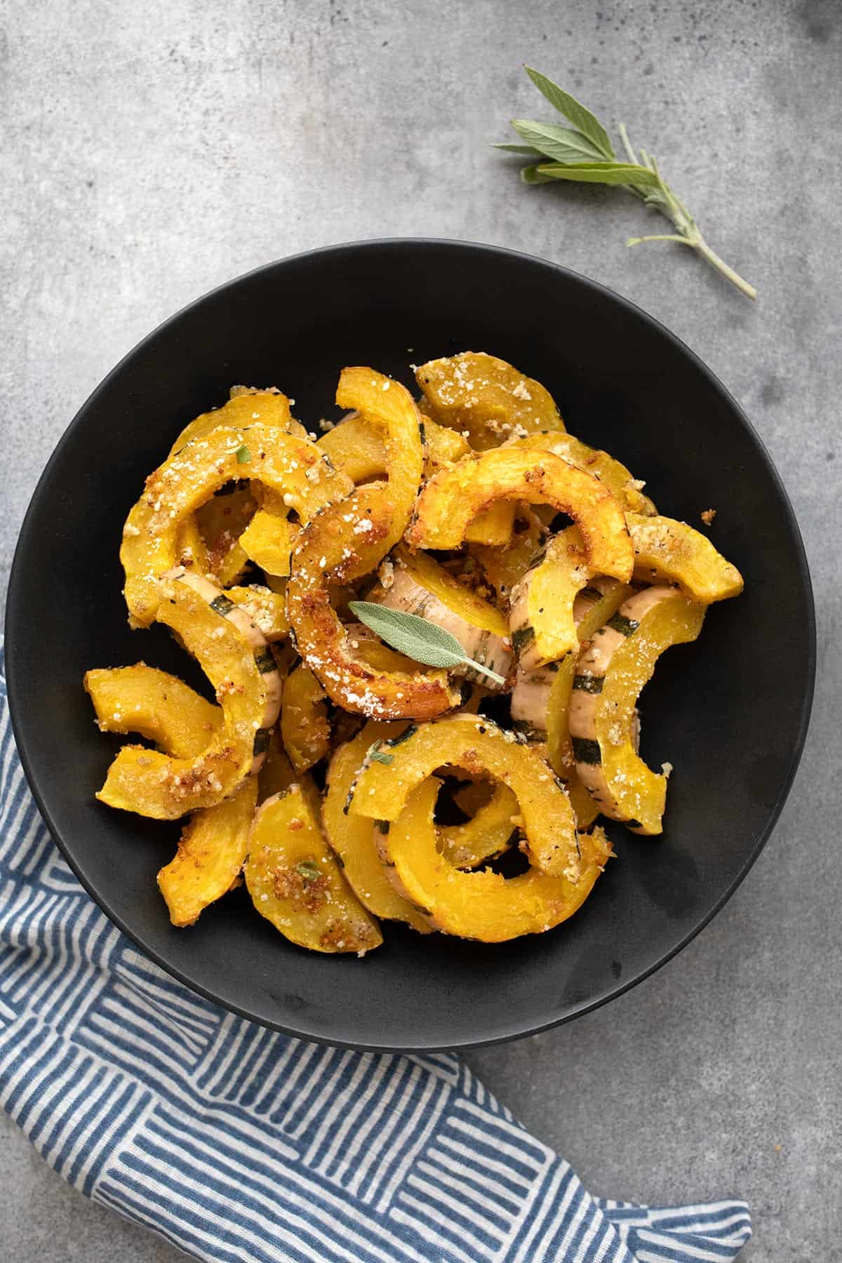 Top down image of Roasted Delicata Squash in a large black bowl on a concrete table.
