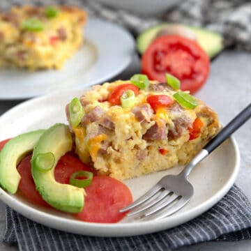 A slice of Slow Cooker Breakfast Casserole on a white plate over a striped grey napkin.