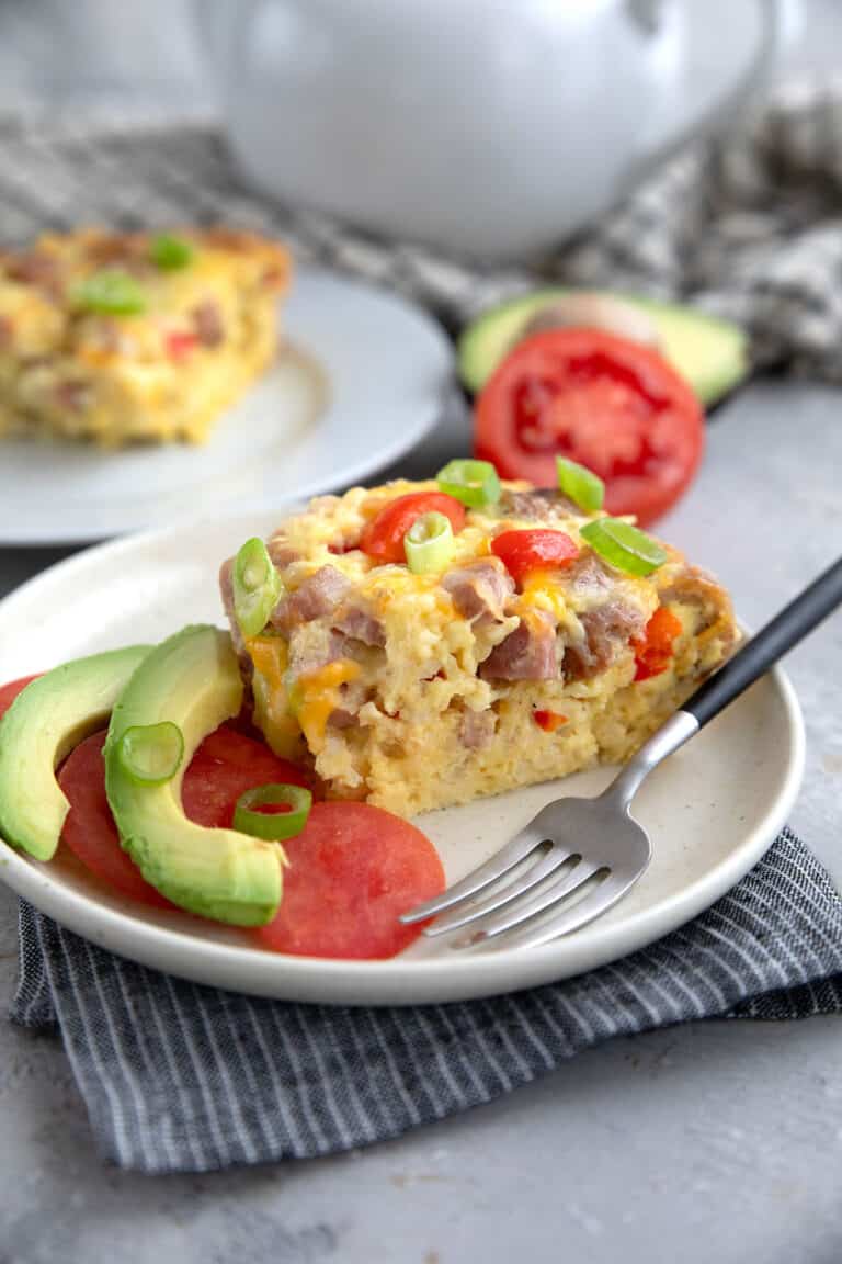 A slice of Slow Cooker Breakfast Casserole on a white plate over a striped grey napkin.