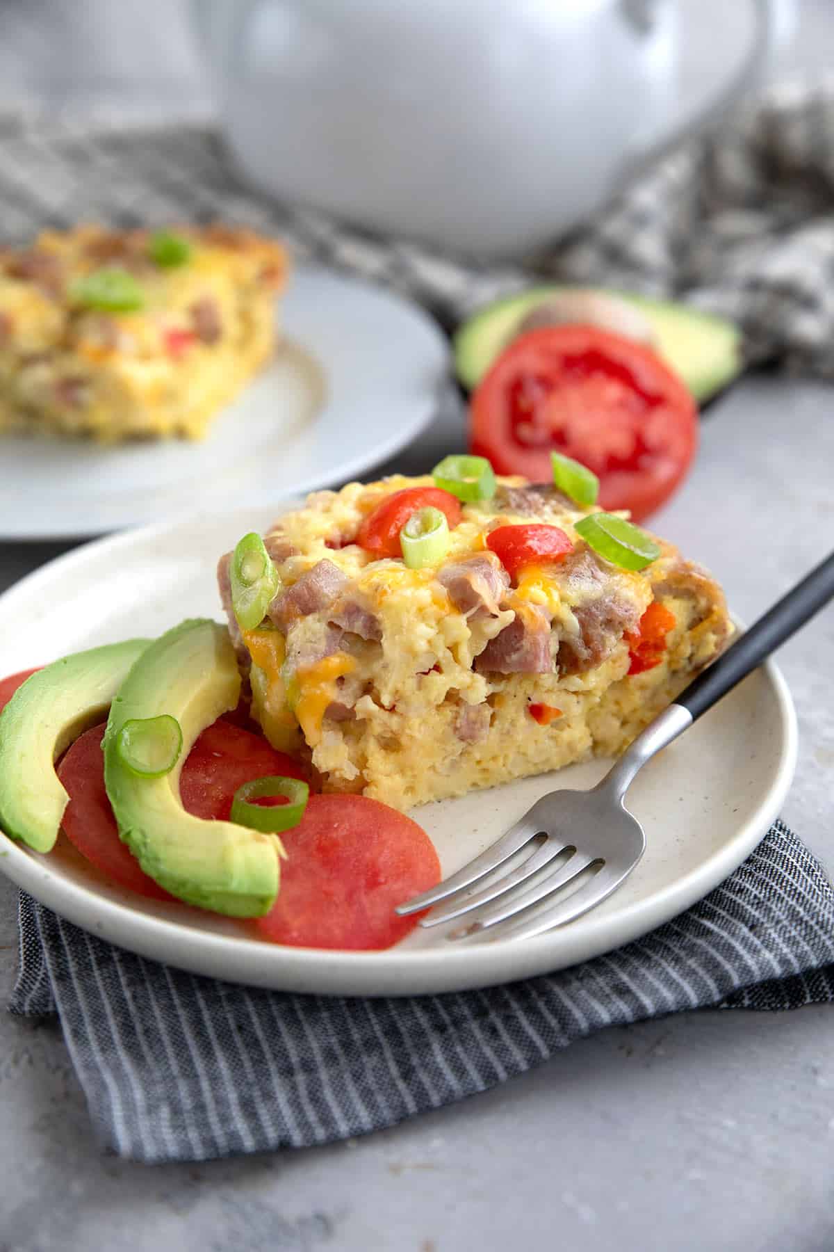 A slice of Slow Cooker Breakfast Casserole on a white plate over a striped grey napkin.