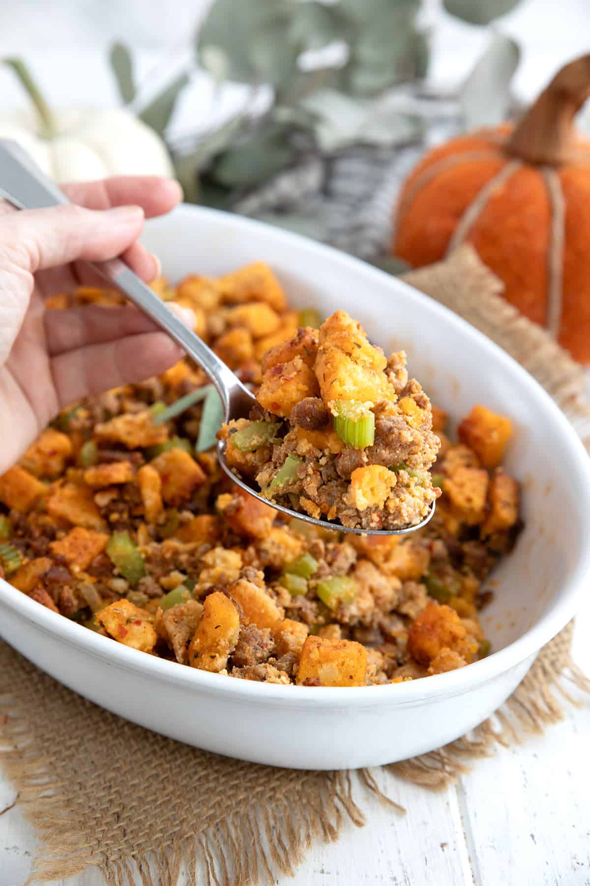 A serving spoon lifting some keto stuffing out of an white oval baking dish.