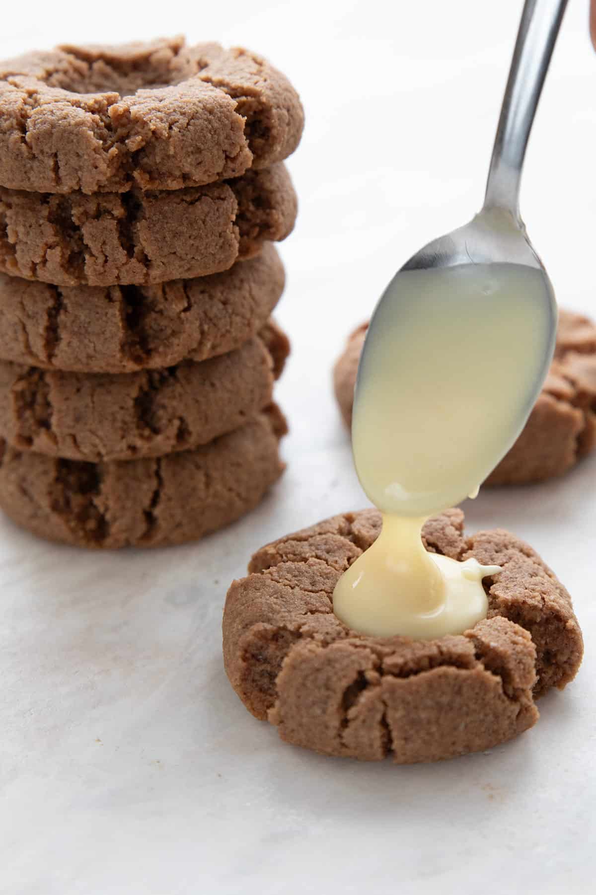 A spoon drizzling sugar free white chocolate into a gingerbread thumbprint.