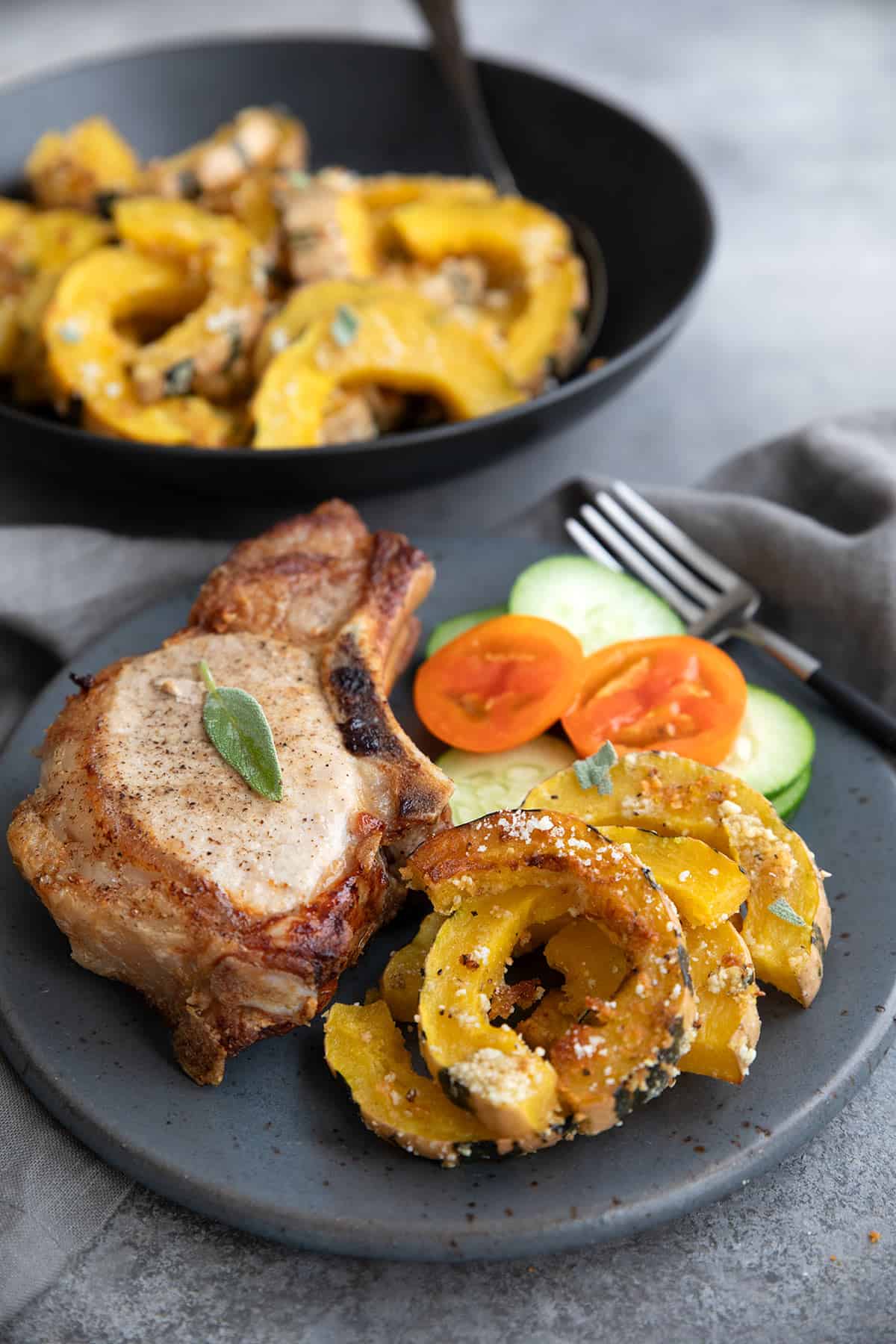 A gray plate with pork chops and Roasted Delicata Squash.
