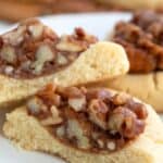 Titled image, close up of a keto pecan pie cookie cut in half on a white plate.