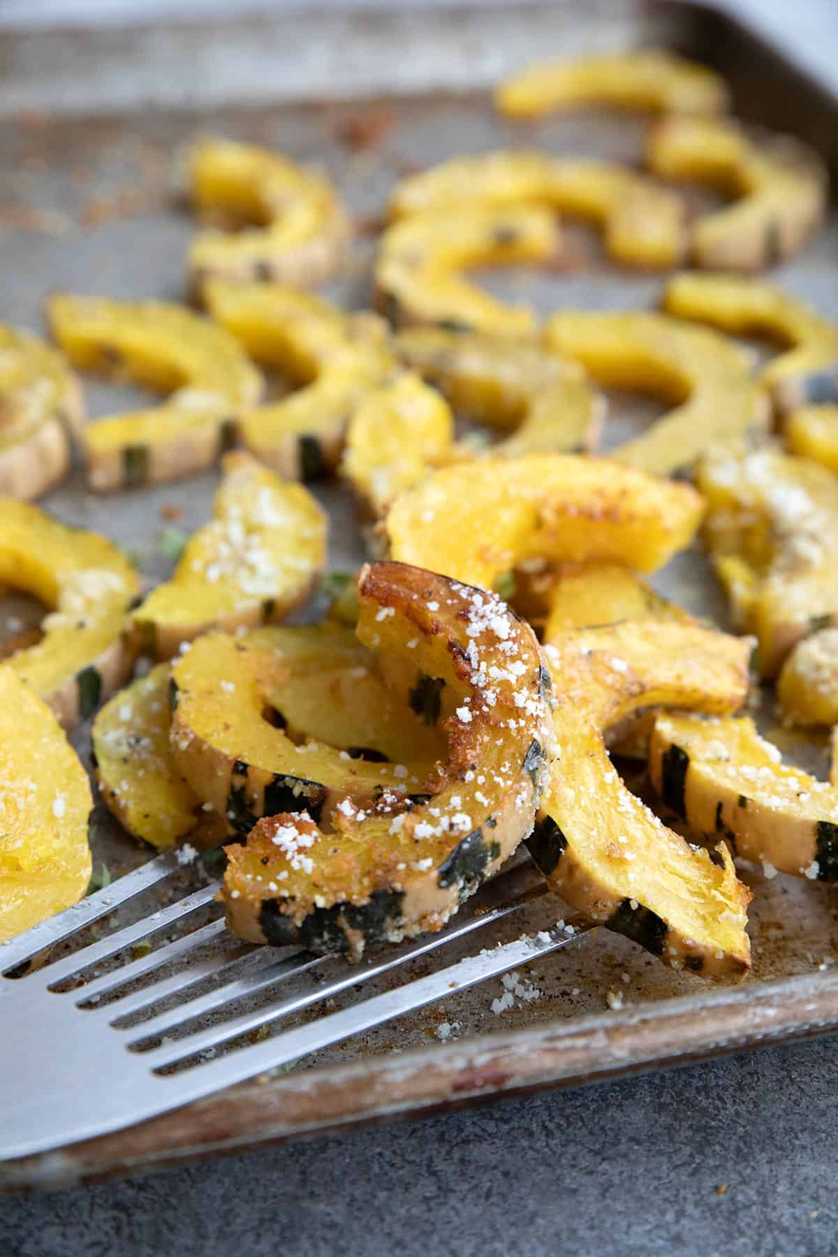 Roasted Delicata Squash on a sheet pan with a spatula lifting up several pieces.