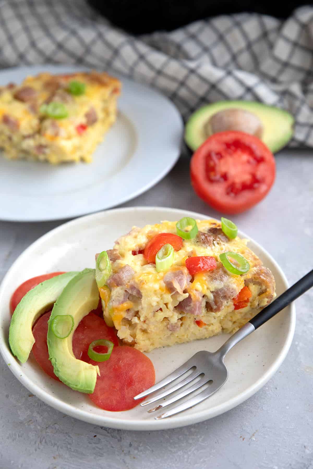 A slice of Slow Cooker Breakfast Casserole on a white plate with some tomato and avocado.