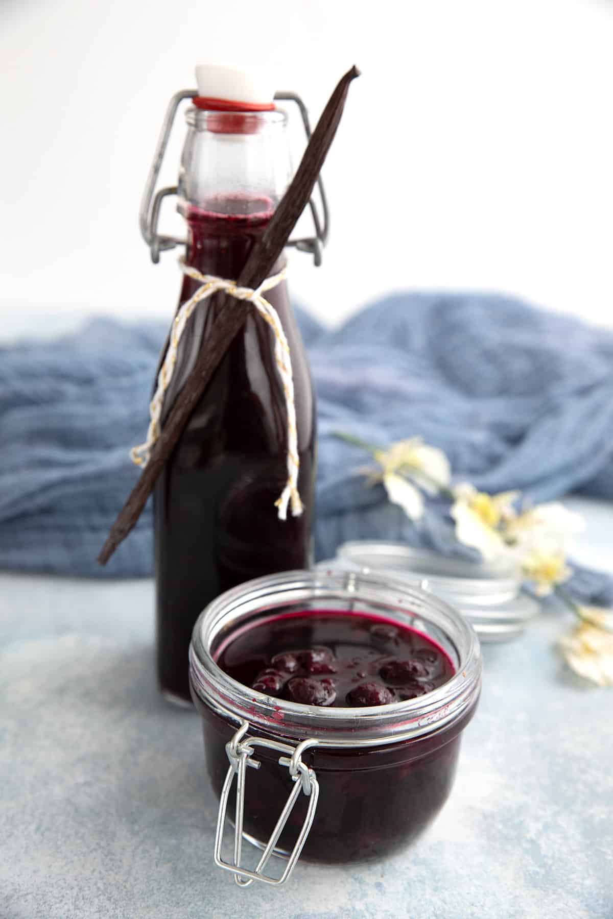 Blueberry syrup in a glass jar with a bottle in behind.