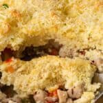 Titled image of a close up of Keto Chicken Pot Pie in the baking dish, with a serving spoon digging into it.