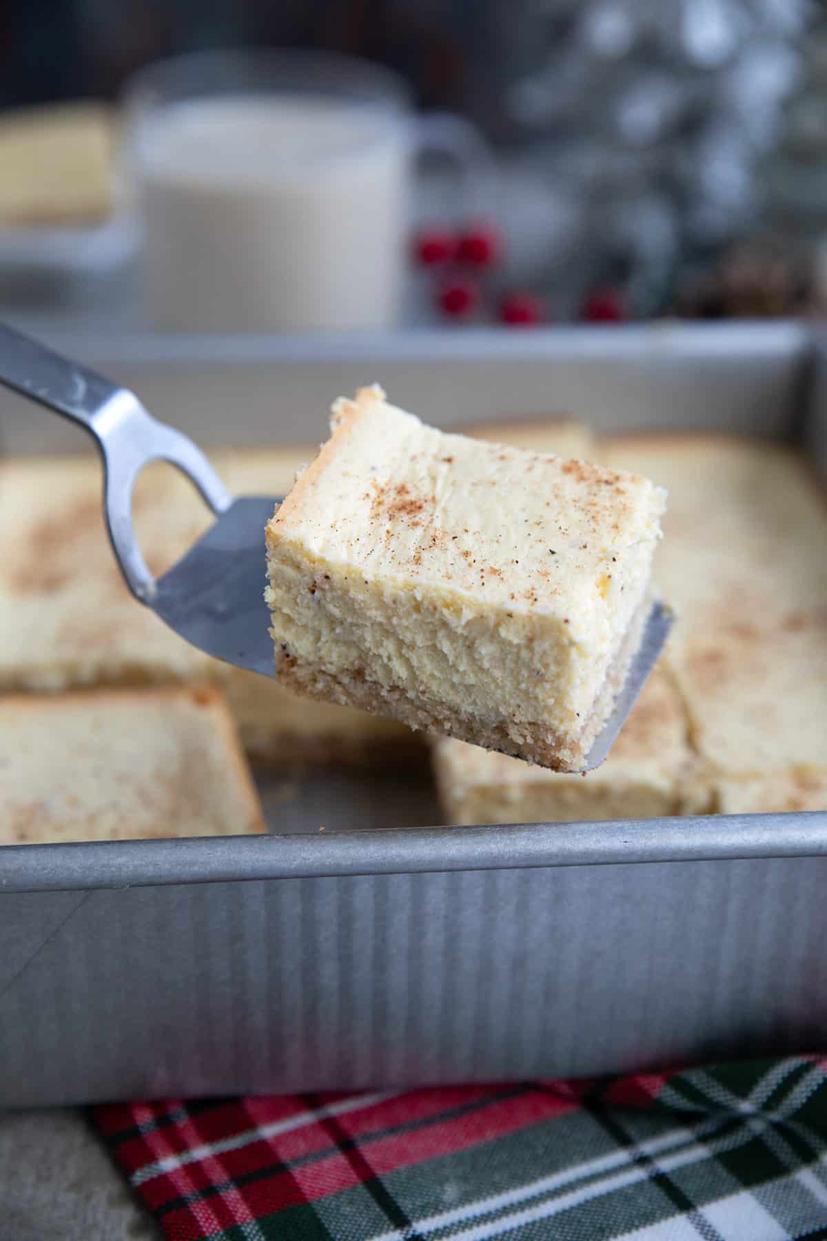 A spatula holding a keto eggnog cheesecake bar above the pan.
