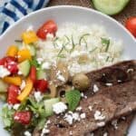 Top down titled image of a white bowl filled with homemade gyro meat, cauliflower rice, and Greek salad.