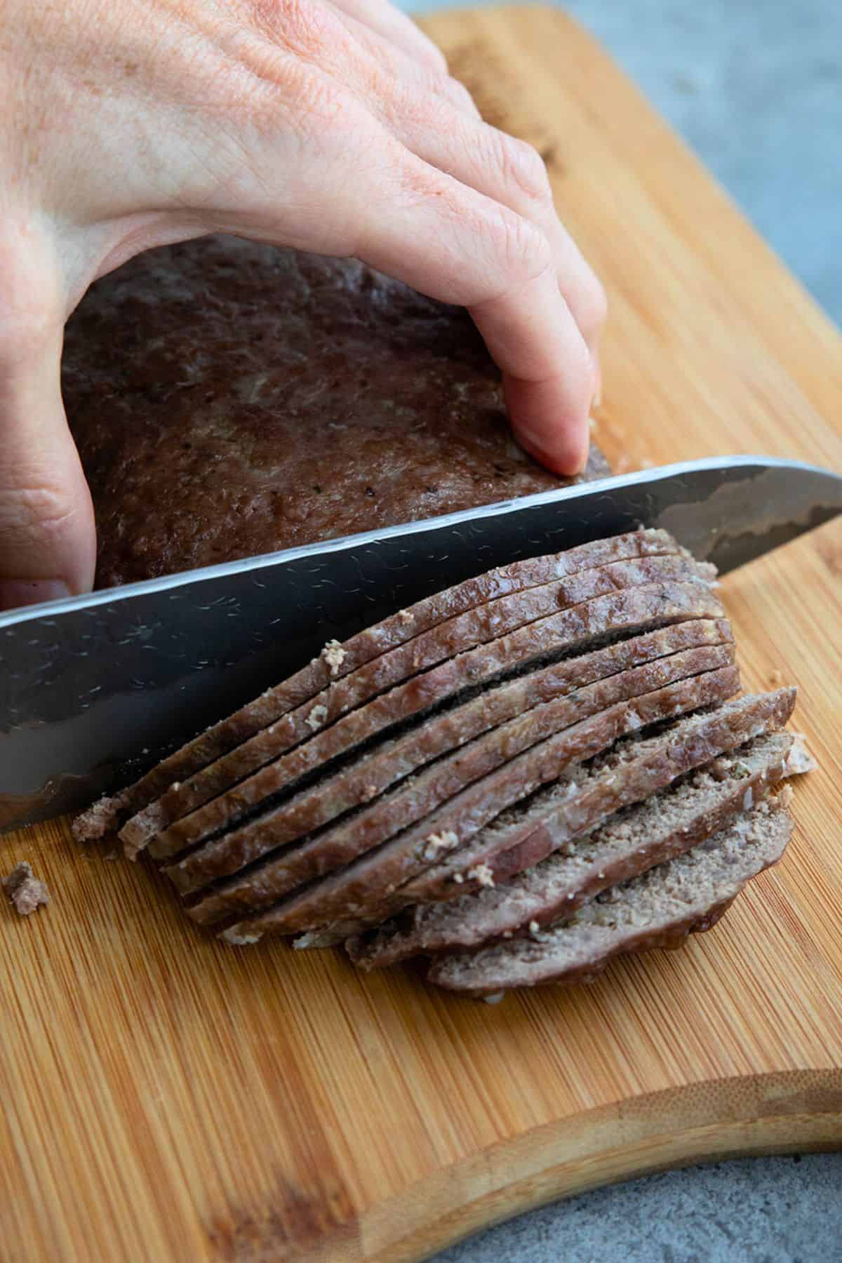 A hand slicing homemade Gyor meat on a cutting board.