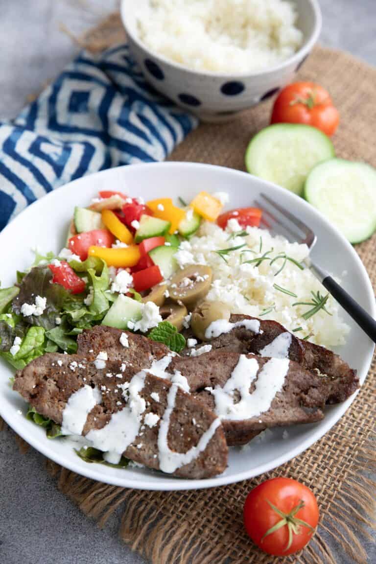 A keto gyro bowl with cauliflower rice and feta dressing in a white bowl.