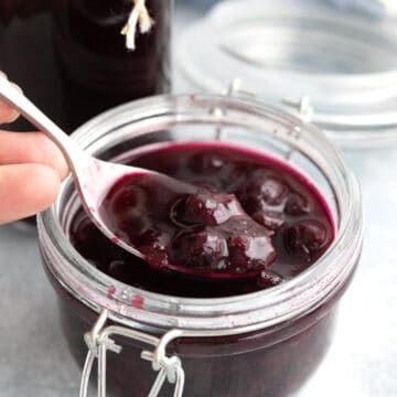 A spoon digging into a jar of blueberry syrup.