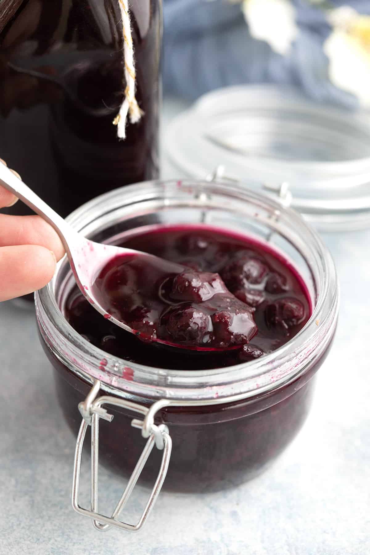 A spoon digging into a jar of blueberry syrup.