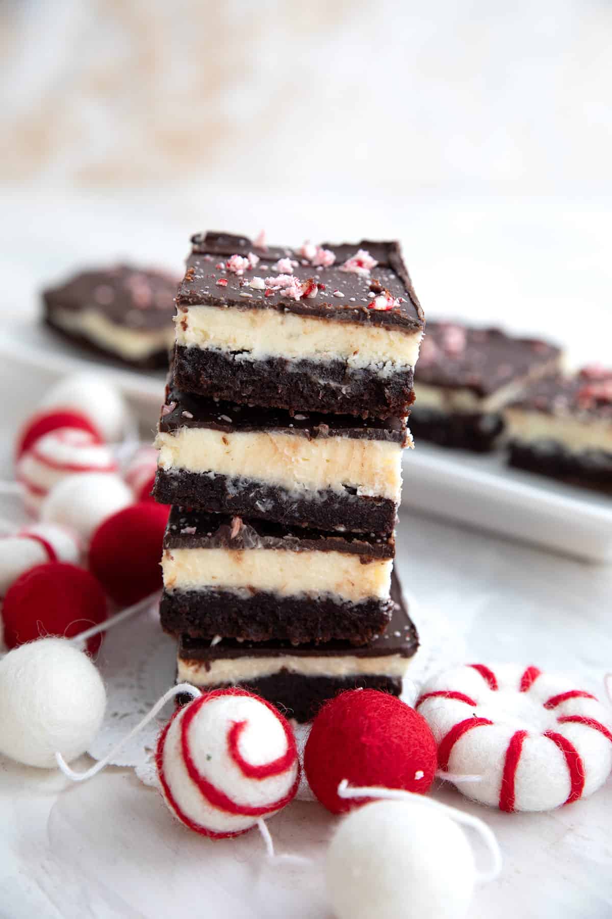 A stack of keto brownies with peppermint frosting on a table with a tray of brownies in the background.