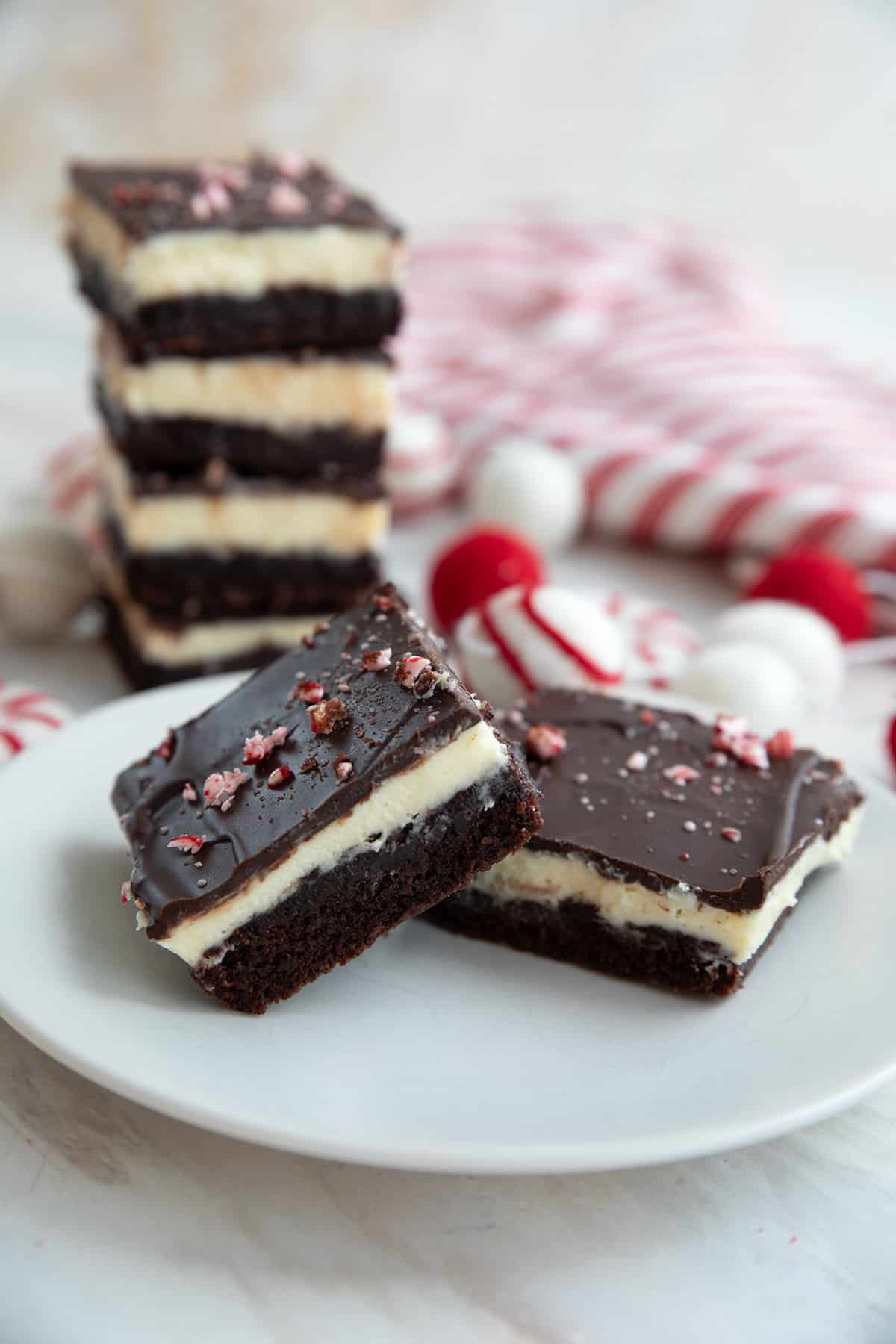 Two keto peppermint brownies on a white plate with a stack of brownies in the background.