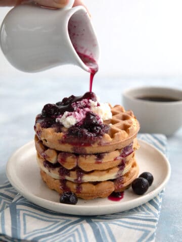 A pitcher pouring keto blueberry syrup over low carb waffles.