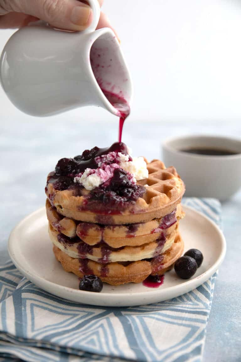 A pitcher pouring keto blueberry syrup over low carb waffles.