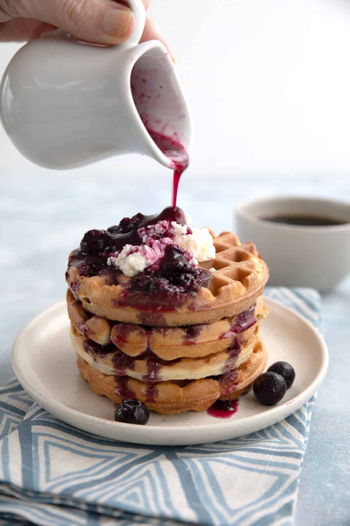 A pitcher pouring keto blueberry syrup over low carb waffles. 