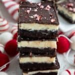 Titled image of a stack of Keto Peppermint Bark Brownies on a white table with small felt Christmas decorations around it.