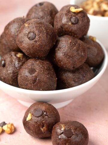 A white bowl filled with chocolate protein balls, with two balls sitting in front.