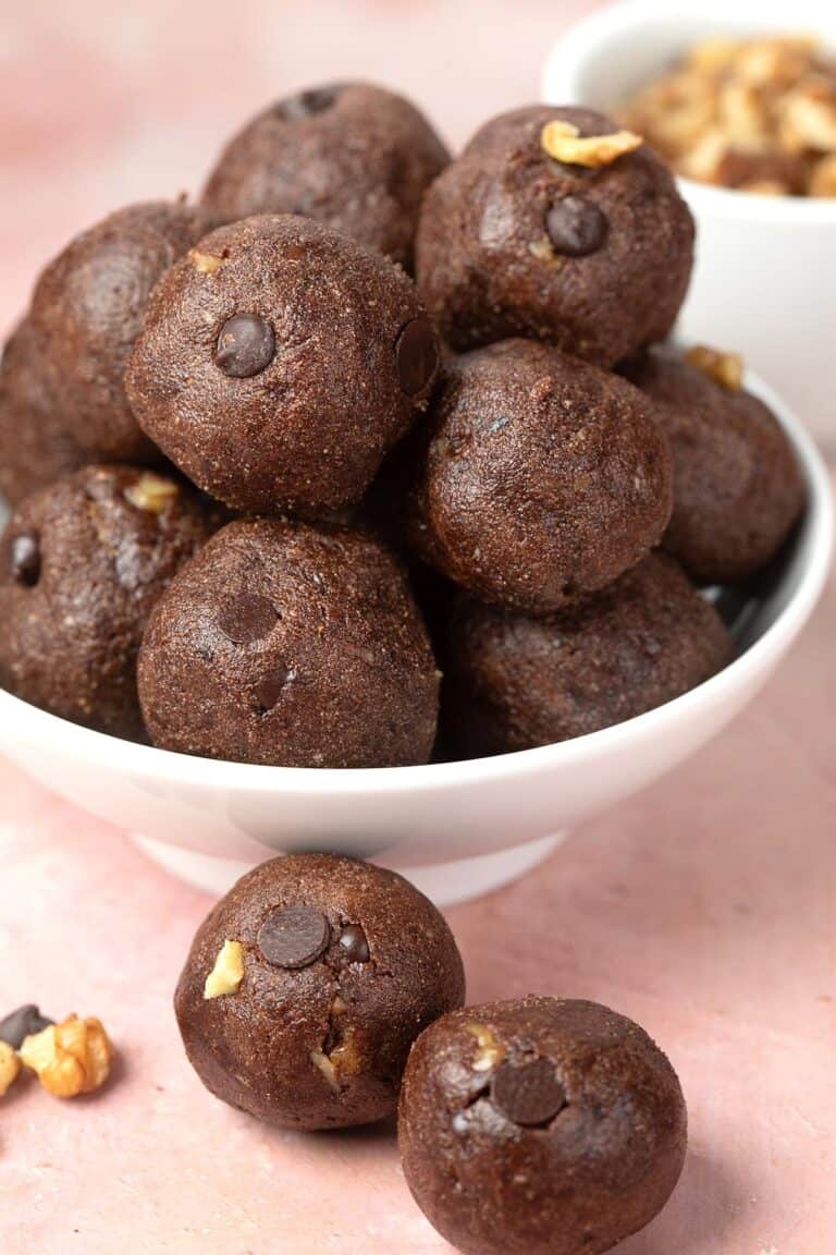 A white bowl filled with chocolate protein balls, with two balls sitting in front.