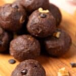 Titled image of chocolate protein balls on a wooden cutting board on a pink background.