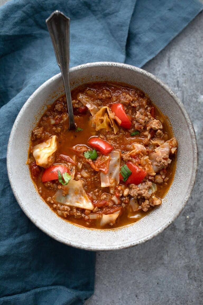 Top down image of Keto Cabbage Soup in a speckled bowl, with a blue napkin underneath.