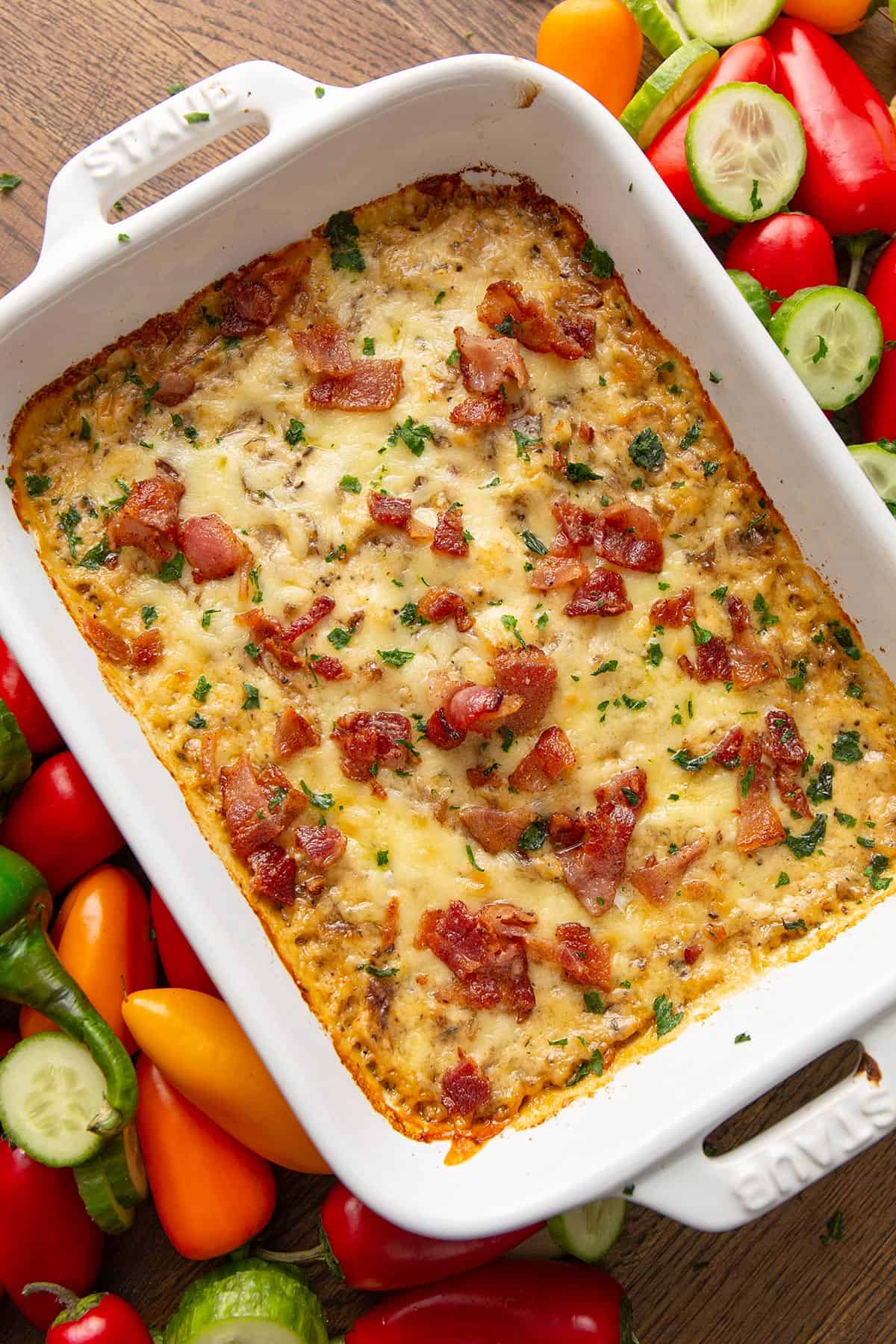 Top down image of Baked Caramelized Onion Dip in a white baking dish, surrounded by vegetables.