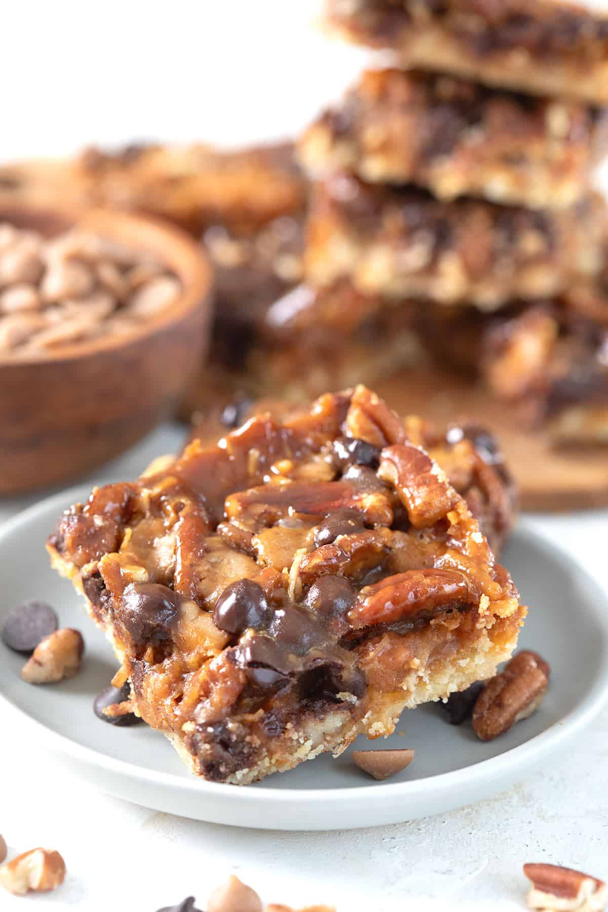 A salted caramel magic bar on a gray plate with chocolate chips and nuts strewn around.