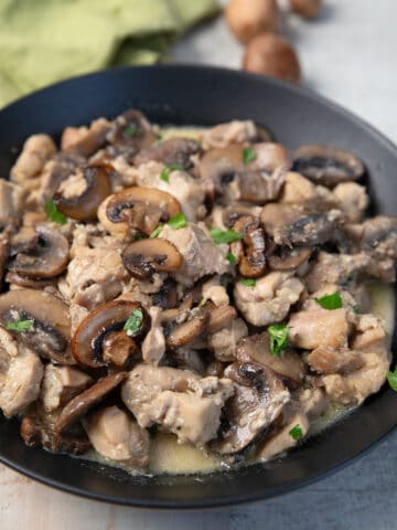 Keto Chicken and Mushrooms in a black bowl with a green napkin and mushrooms in the background.