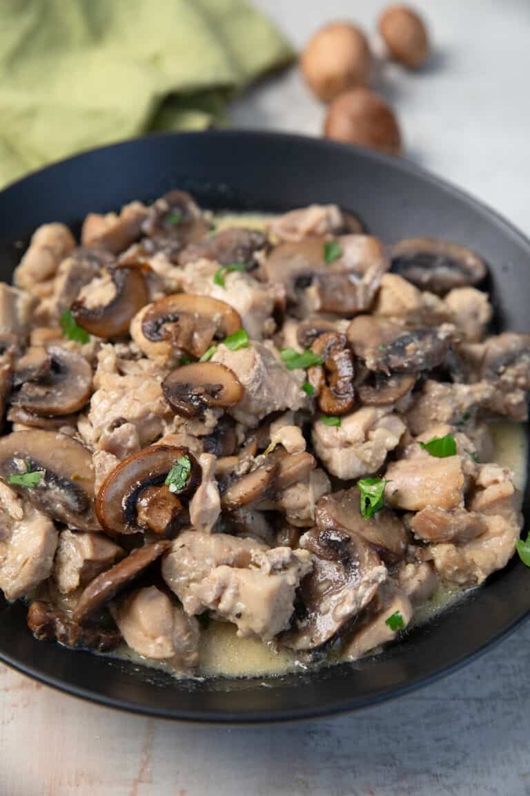 Keto Chicken and Mushrooms in a black bowl with a green napkin and mushrooms in the background.