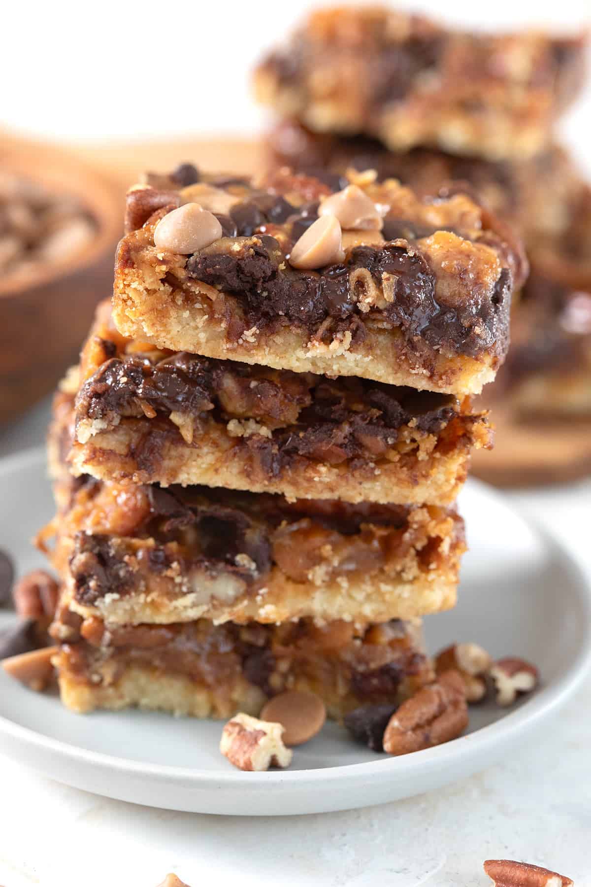 A stack of keto magic cookie bars with nuts and chocolate chips strewn around.