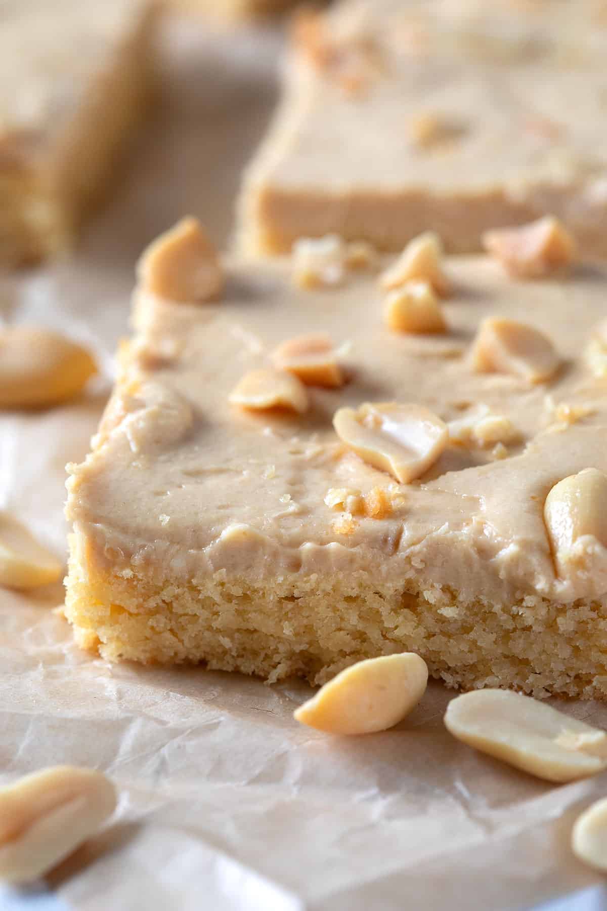 Close up shot of a slice of Keto Peanut Butter Sheet Cake with peanuts strewn around.