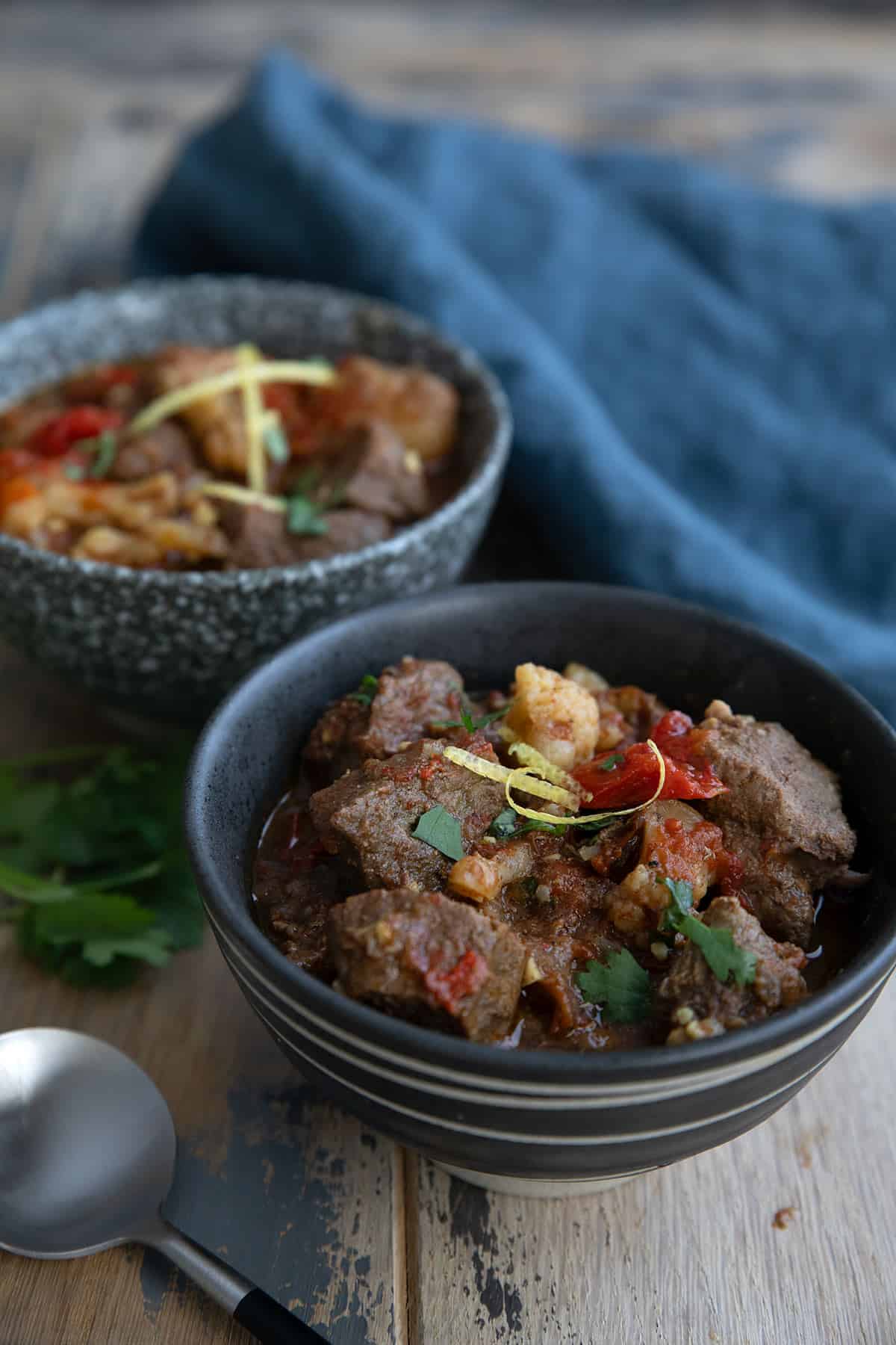 Two bowls of keto lamb stew on a wooden table with a blue napkin in behind.