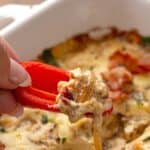 A hand digging a piece of red pepper into Baked Caramelized Onion Dip.