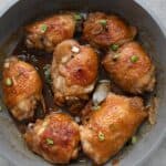 Top down image of chicken adobo in the pan with green onion sprinkled on top.