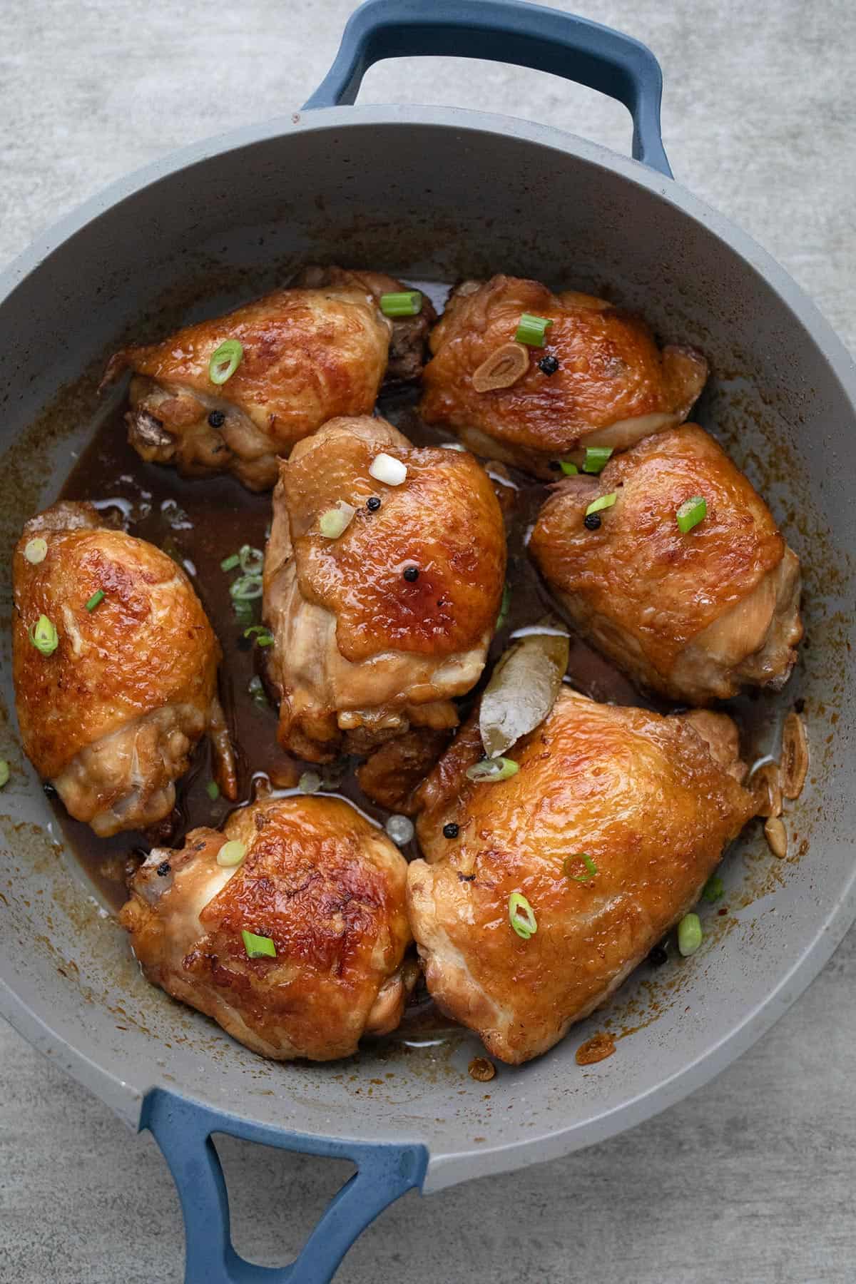 Top down image of chicken adobo in the pan with green onion sprinkled on top.