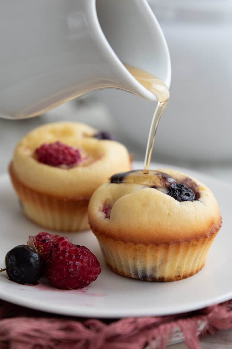 Syrup being drizzled over Keto Pancake Muffins on a white plate.