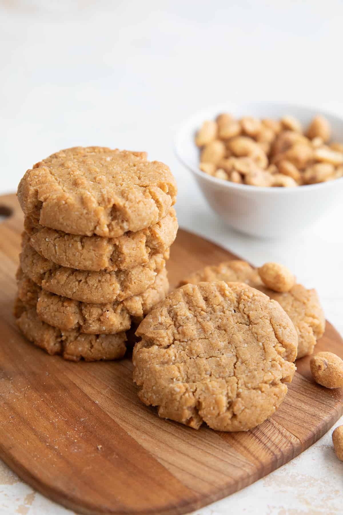Keto Peanut Butter Cookies on a small cutting board with peanuts in the background.