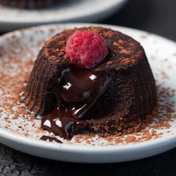 A Keto Air Fryer Lava Cake on a white plate with a raspberry on top, with the lava oozing out.