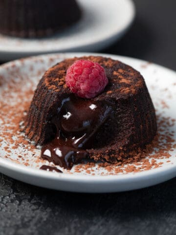A Keto Air Fryer Lava Cake on a white plate with a raspberry on top, with the lava oozing out.