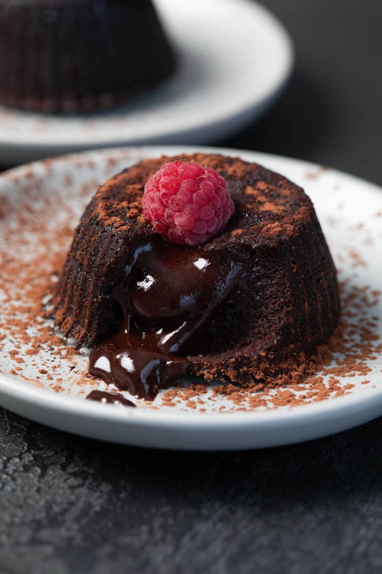 A Keto Air Fryer Lava Cake on a white plate with a raspberry on top, with the lava oozing out.