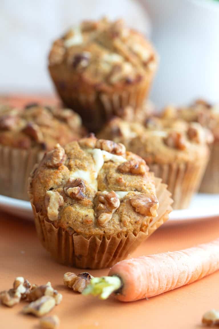 A plate of cream cheese filled Carrot Cake Muffins on an orange tabletop.