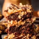 Titled image of a stack of German Chocolate Keto Brownies on a dark background.